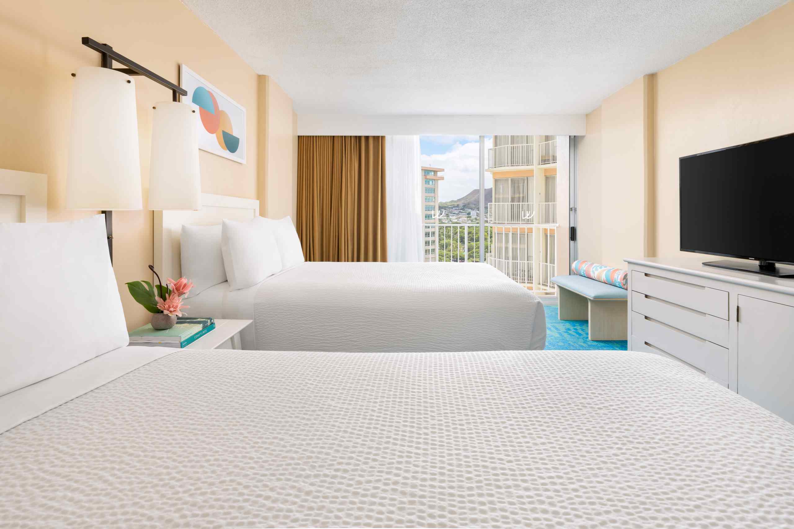 A hotel room with a city view, featuring twin beds, a flat-screen TV, and balcony access.