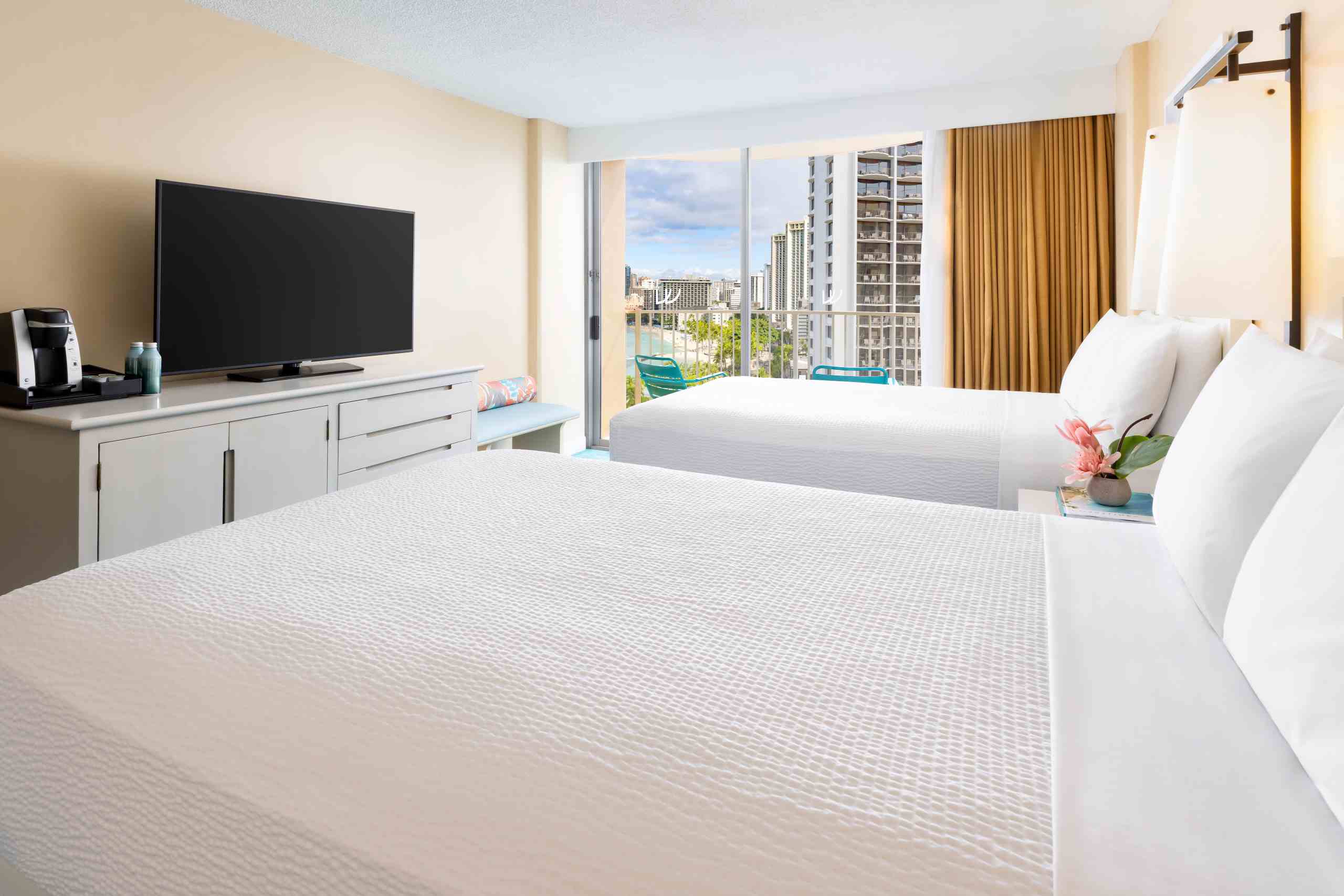 A hotel room with two beds, a TV, and a balcony with a city view.