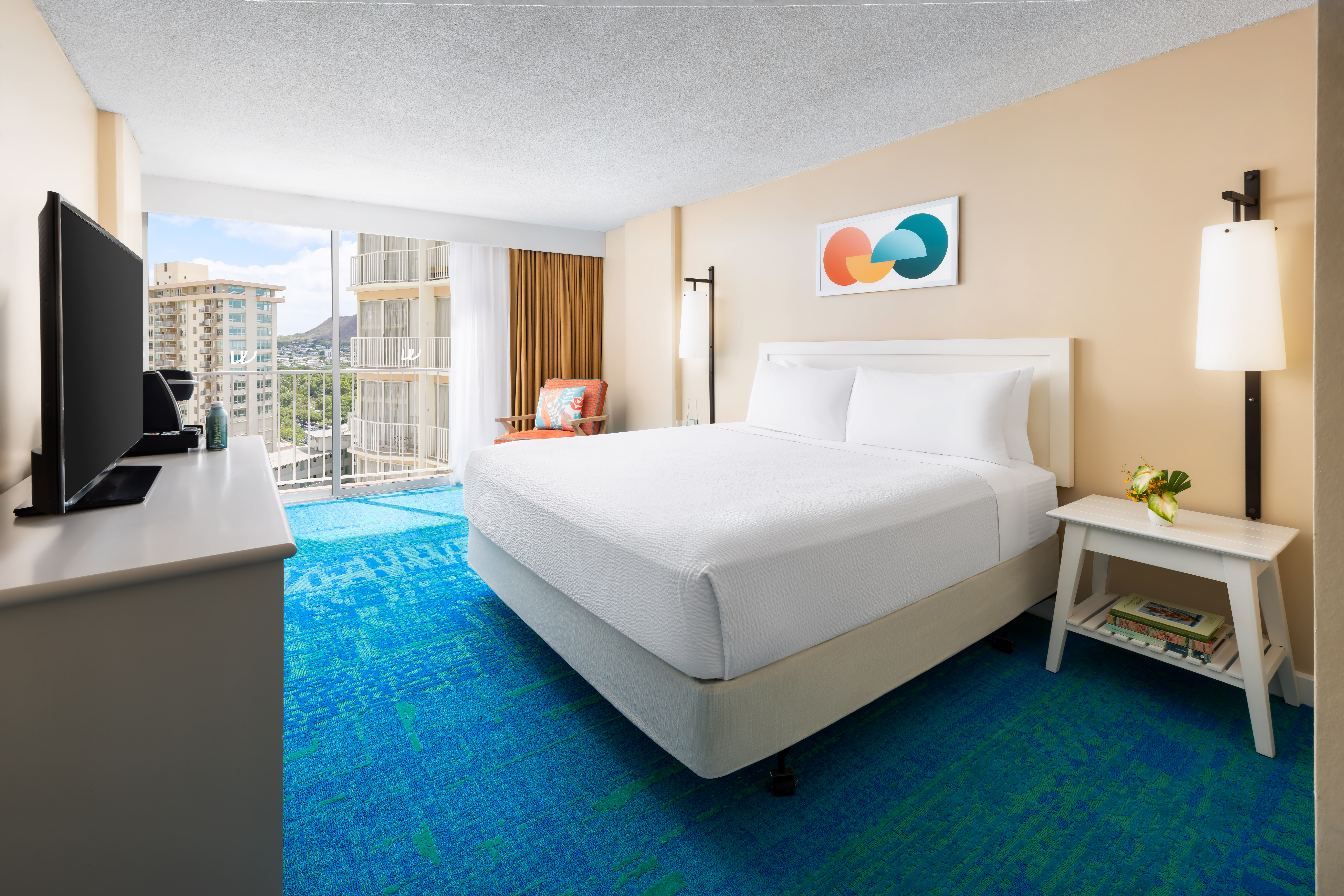 A hotel room with a large bed, blue carpet, and balcony with a city view.