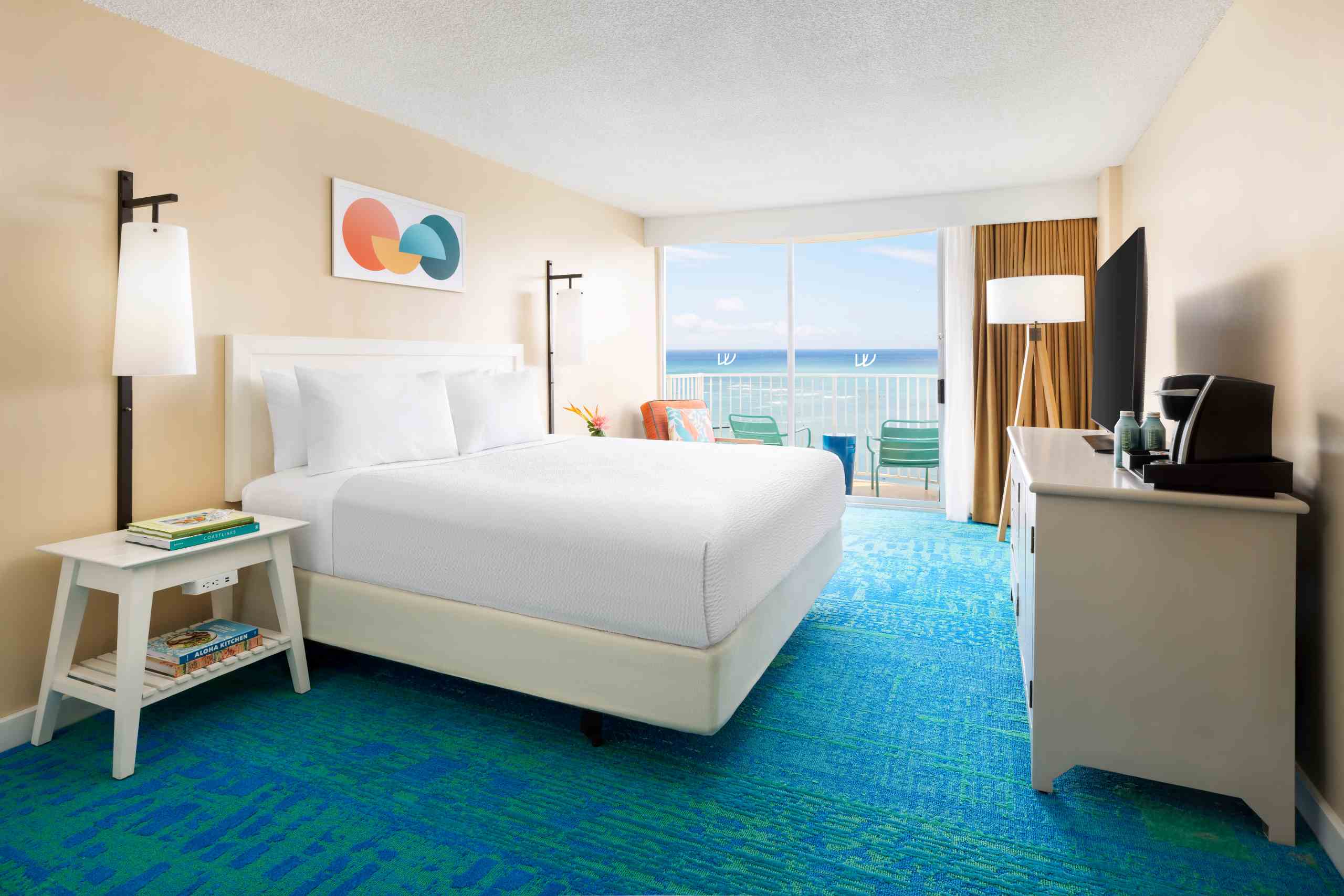 A hotel room with a king-sized bed, balcony, ocean view, TV, and desk.