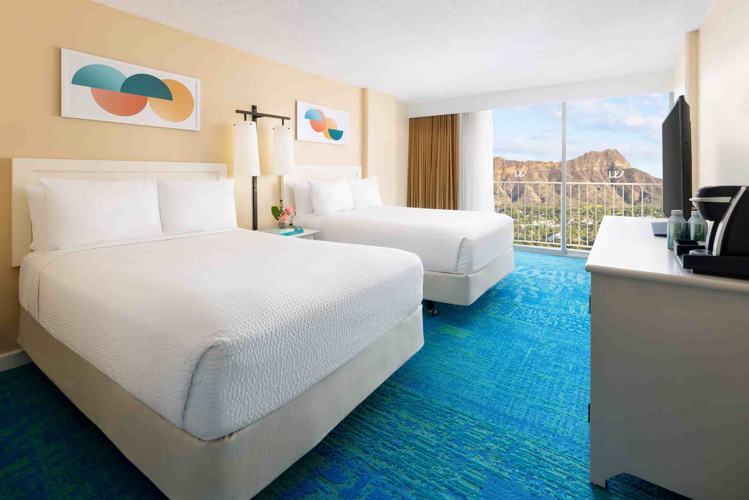 A hotel room with two beds, blue carpet, a balcony, and a mountain view.