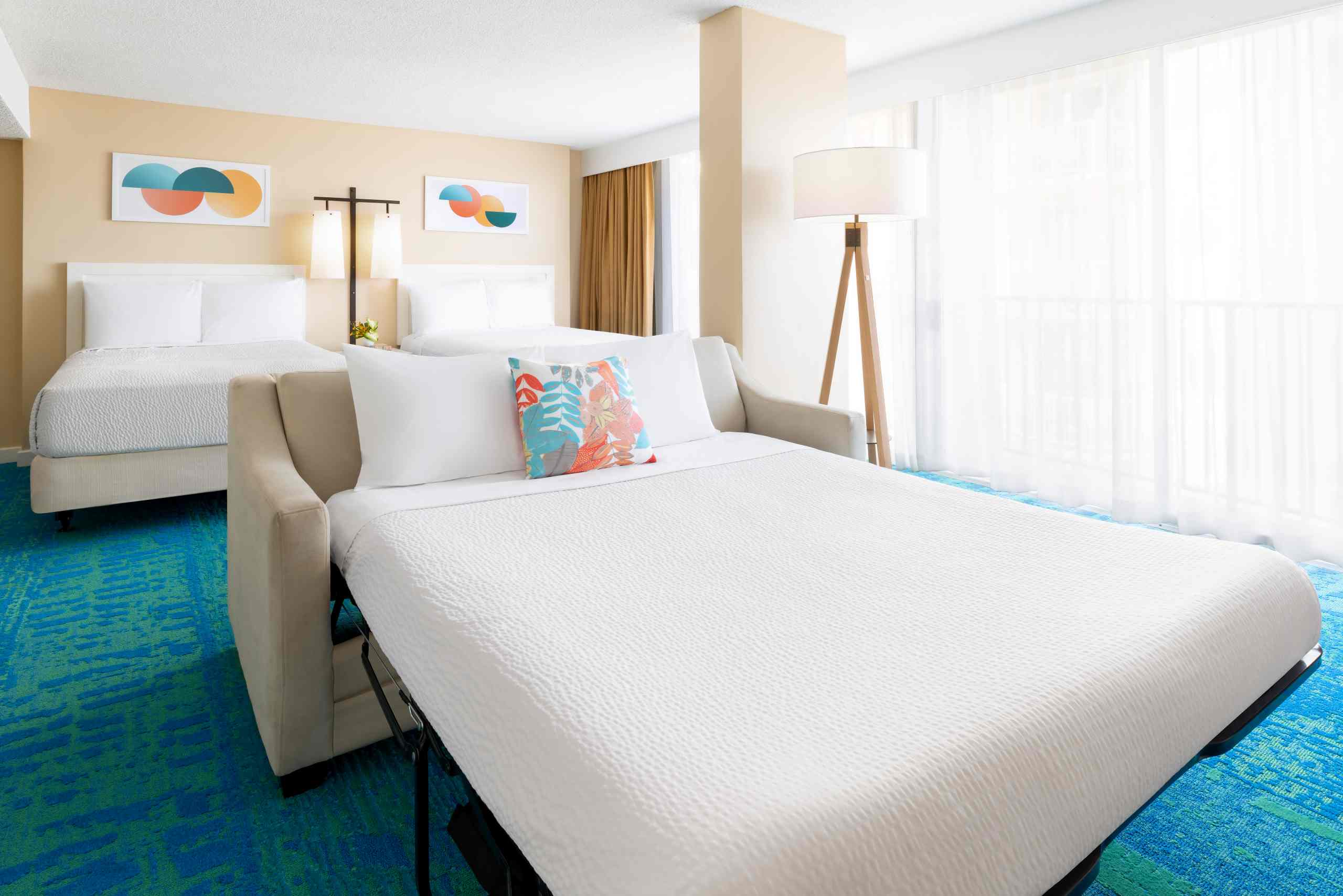 A hotel room with a sofa bed, double bed, and large window with curtains.