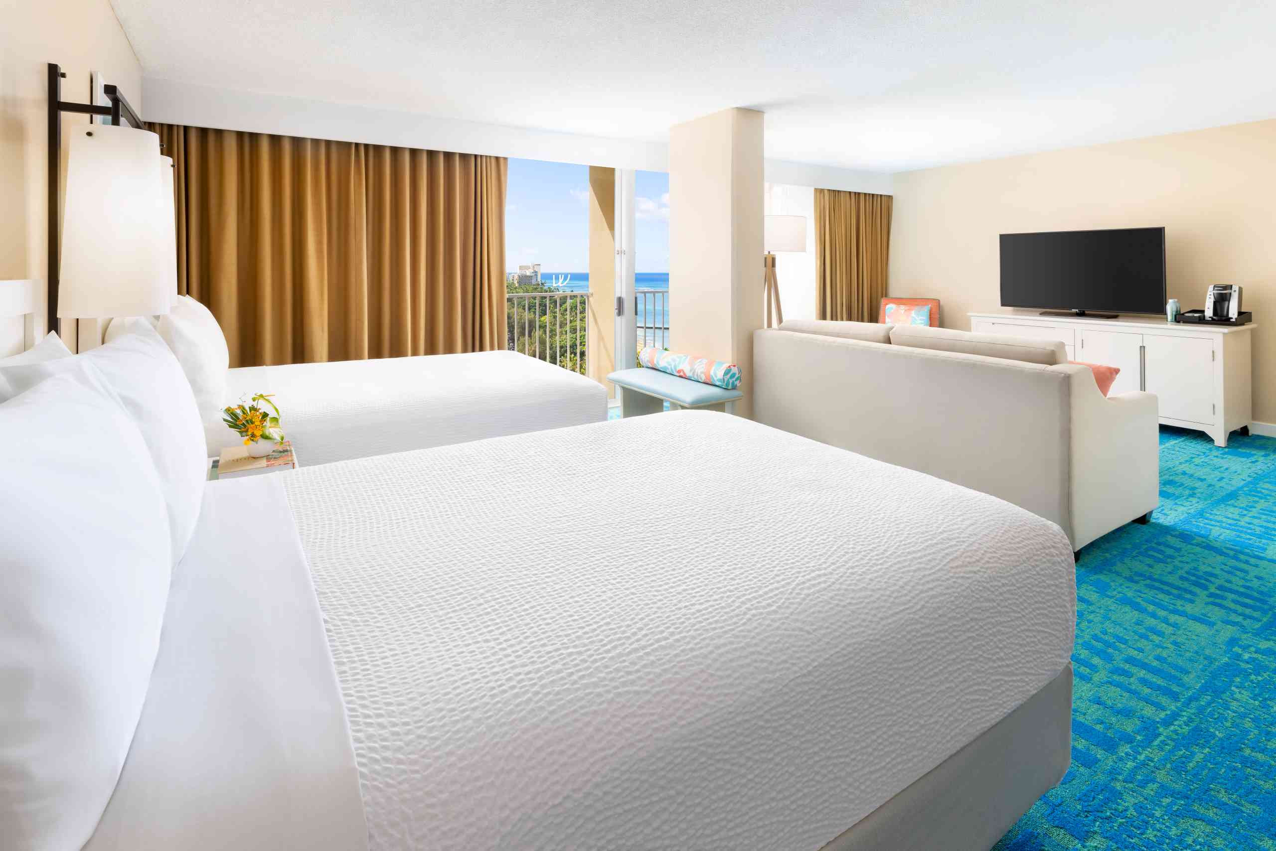 A hotel room with a partial ocean view, featuring two beds, a sofa, and a flat-screen TV.