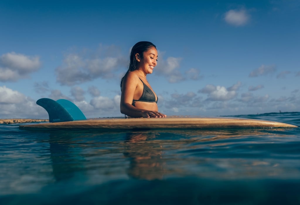 A woman in a bikini enjoying the Hawaiian ocean waves while sitting on a surfboard.