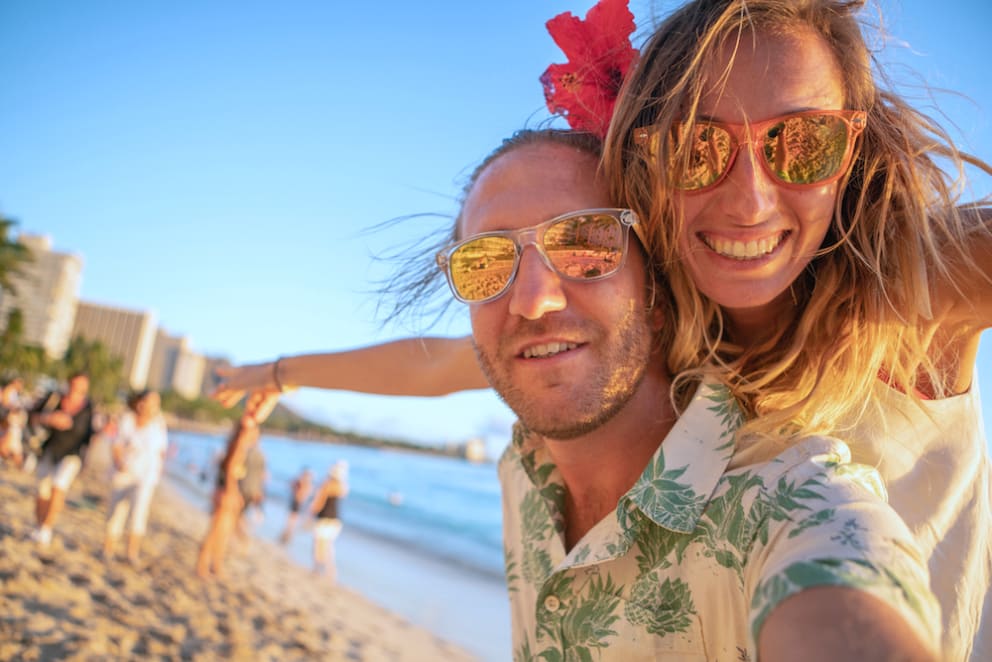 A couple smiling while taking a selfie on a Twin Fins beach with the ocean waves in the background.