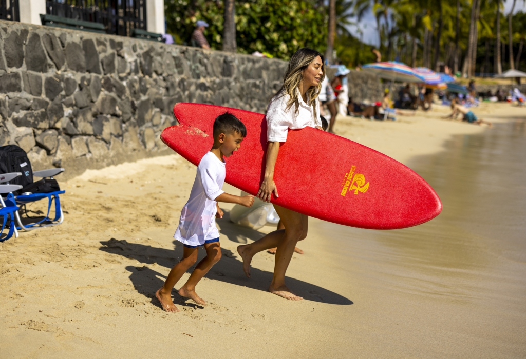 Mother and son carrying surfboard on beach