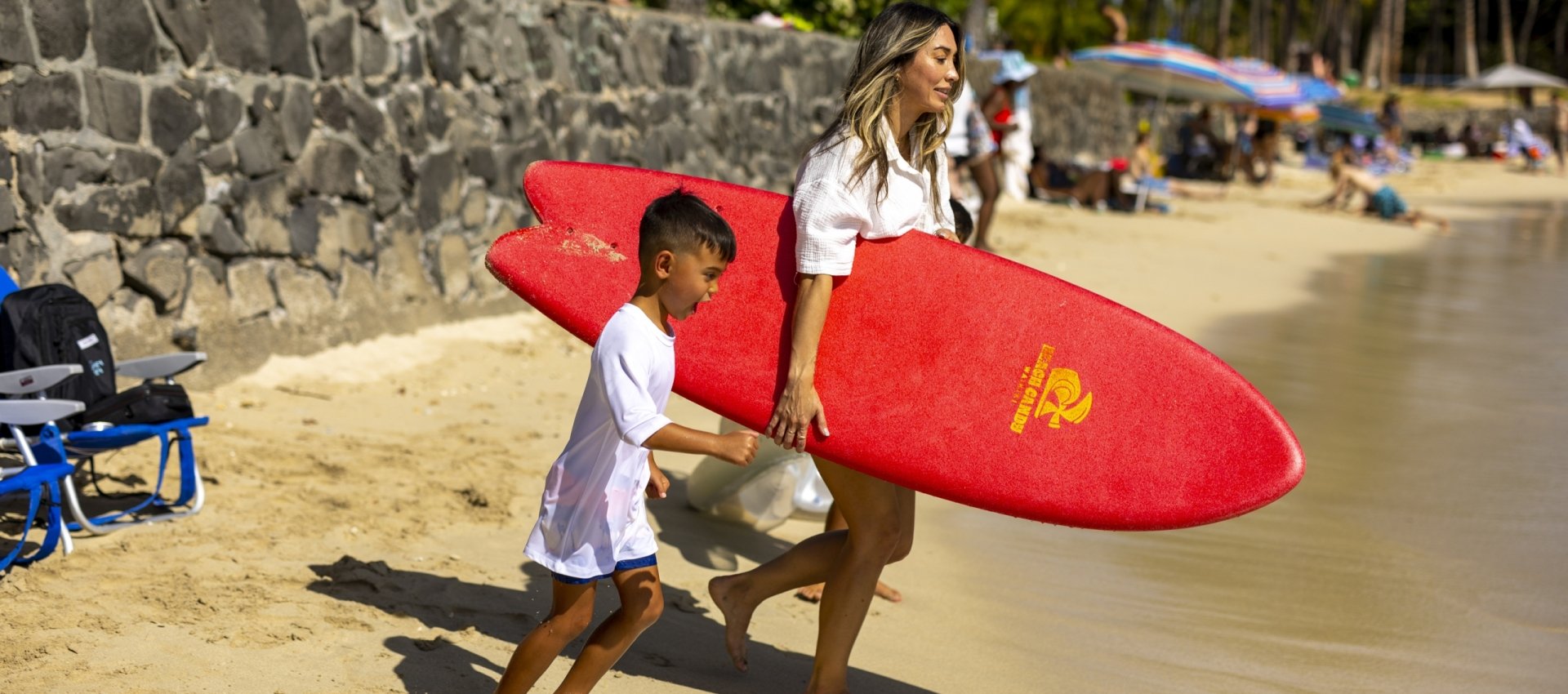 Mother and son carrying surfboard on beach