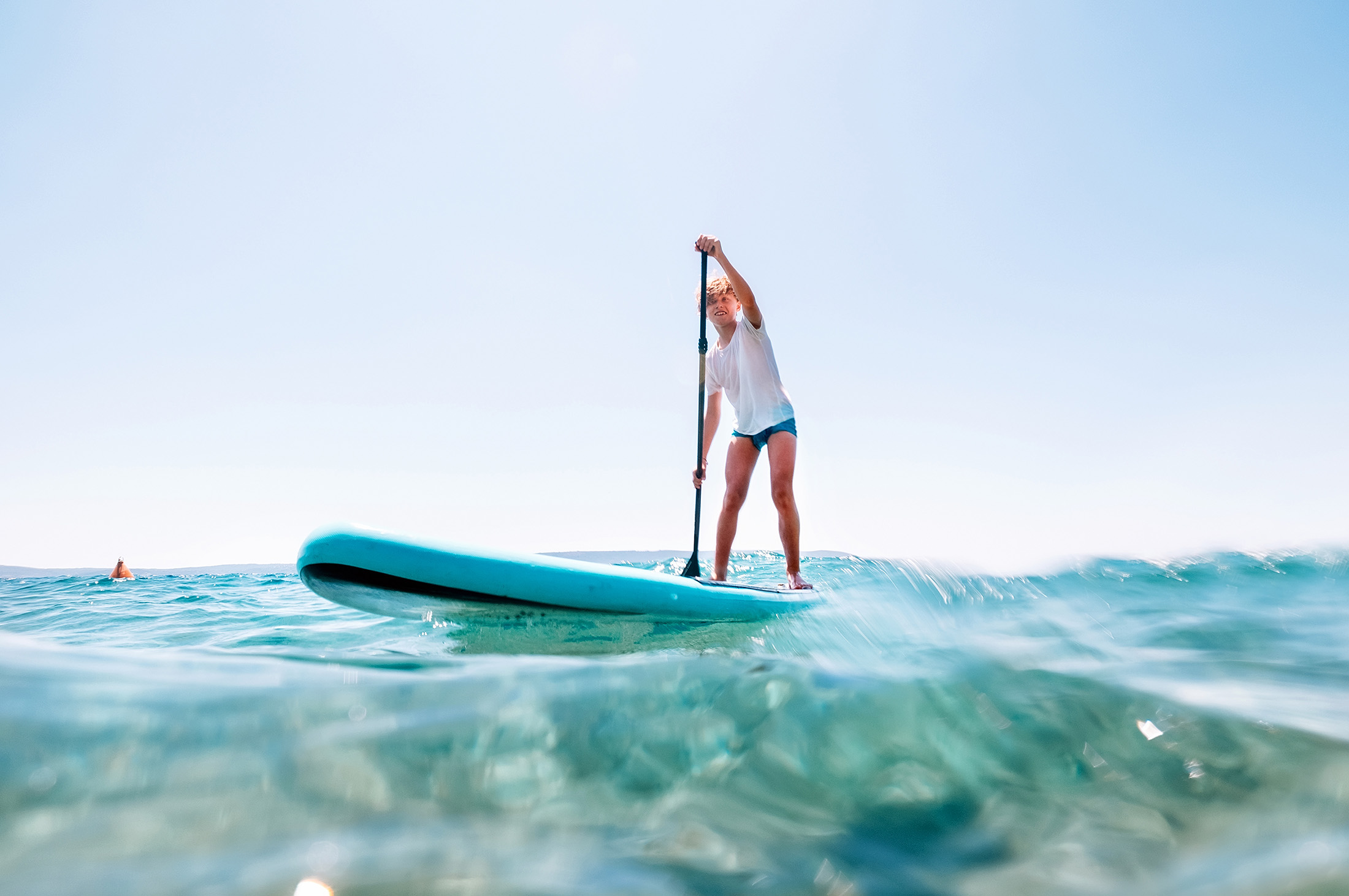 A child enjoys paddle boarding in the ocean near Twin Fin