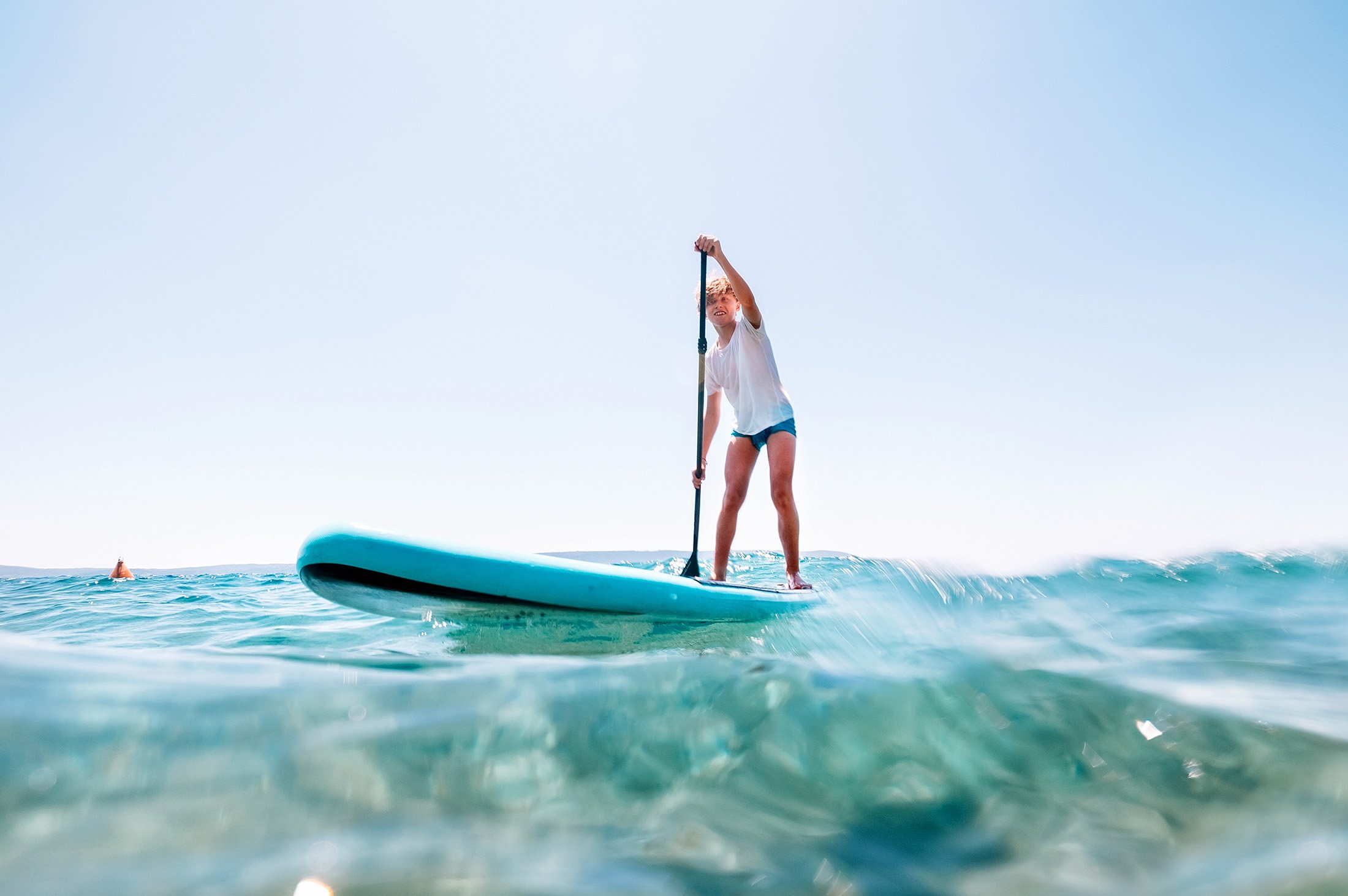 A young girl confidently stands on a paddle board, gracefully gliding across the serene ocean waters.