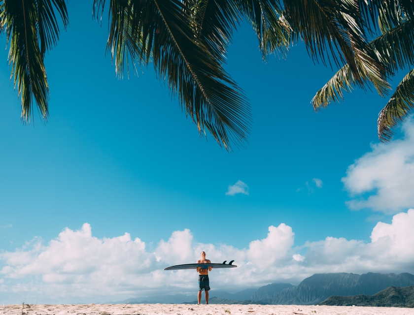 Person holding surfboard parallel to the beach