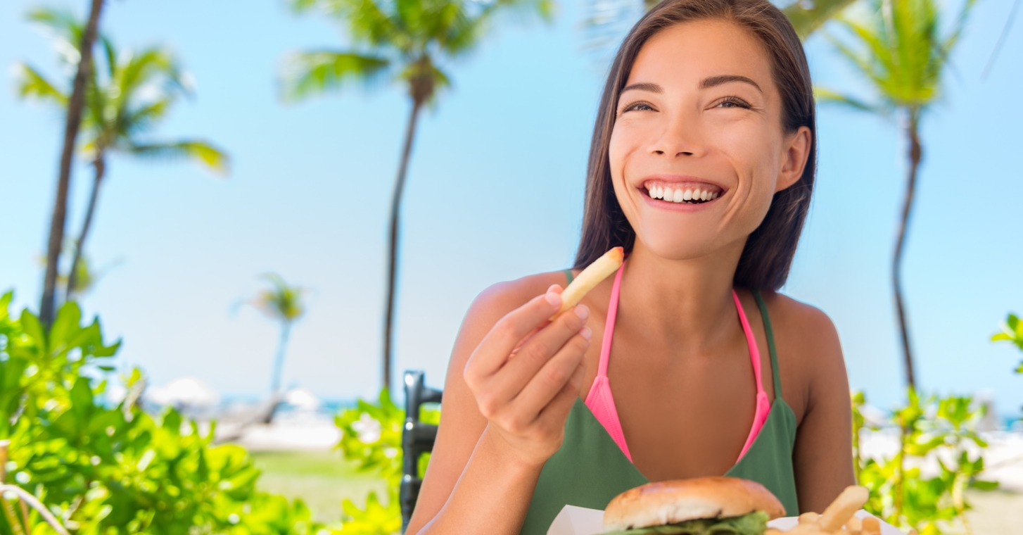 Woman eating burger and fries with beach in background
