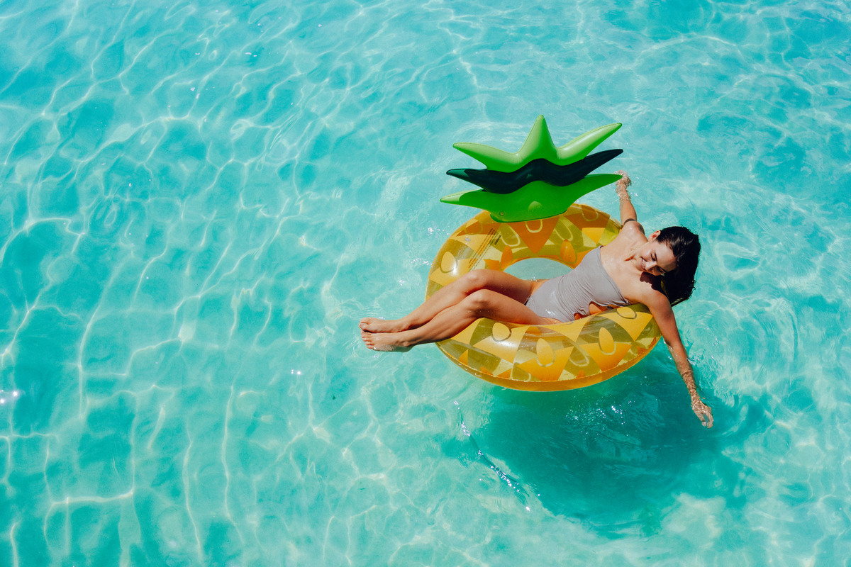 A woman relaxes on an inflatable pineapple float in a pool.