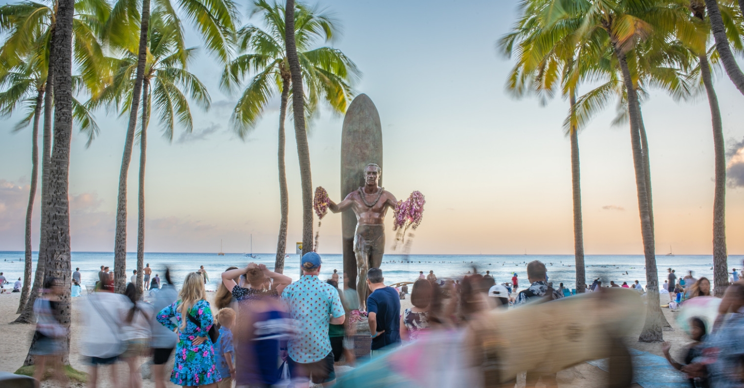 Crowd of tourists gather around Duke Kahanamoku Statue in Oahu Waikiki