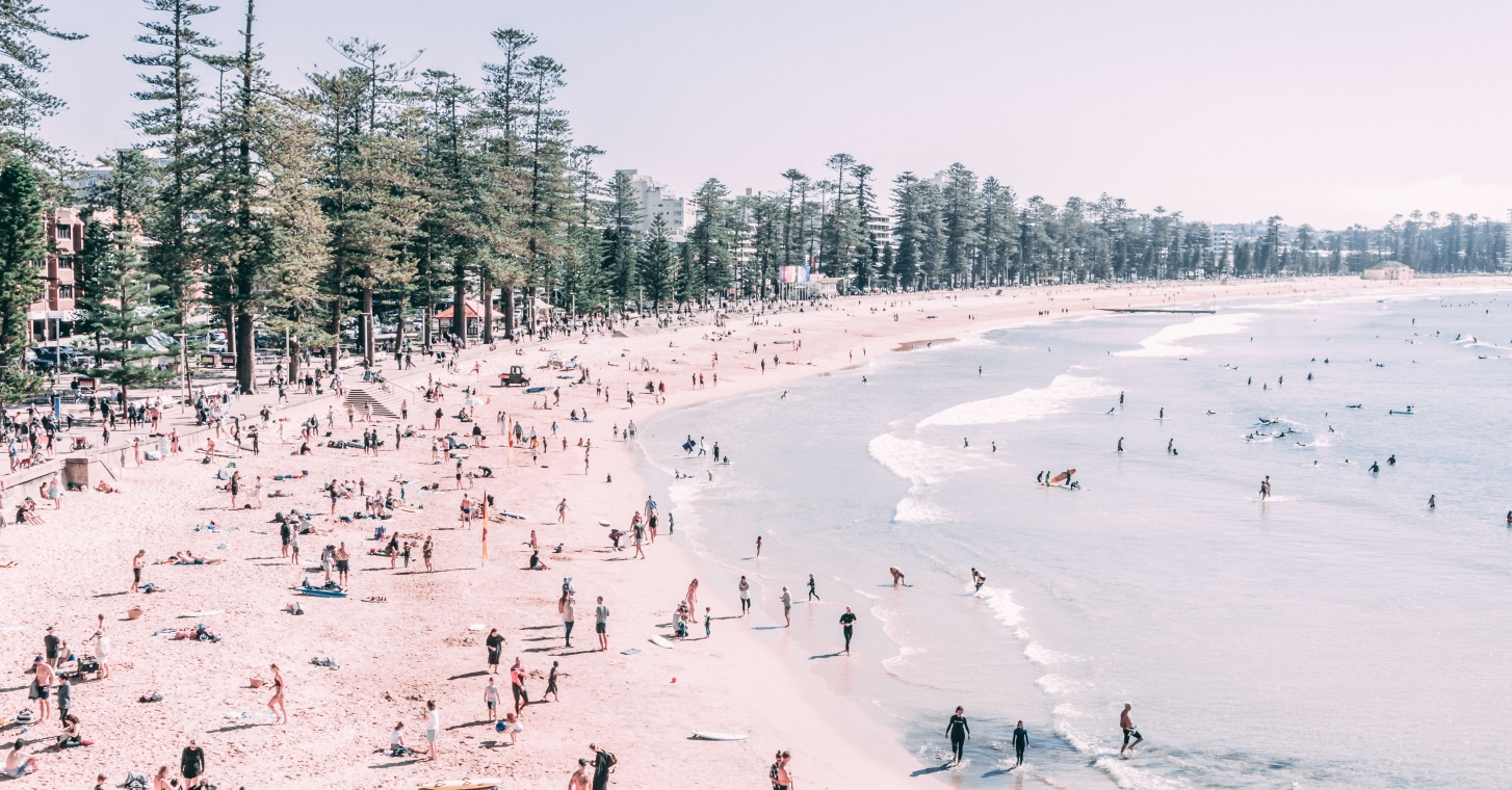 Manly Beach featuring numerous people enjoying the sun and sand playing, and relaxing.