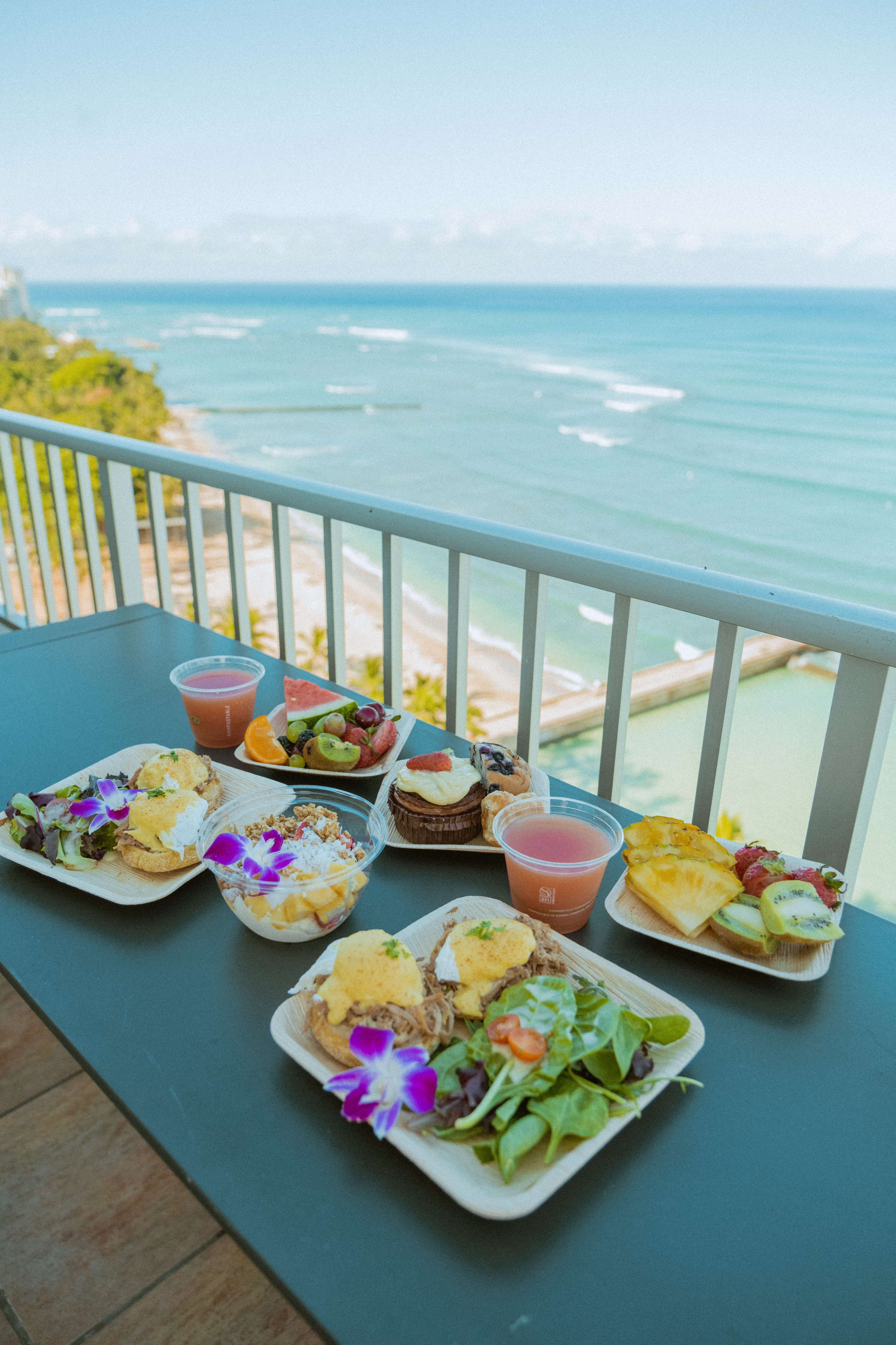 A table with food and drinks on a balcony overlooking the ocean.