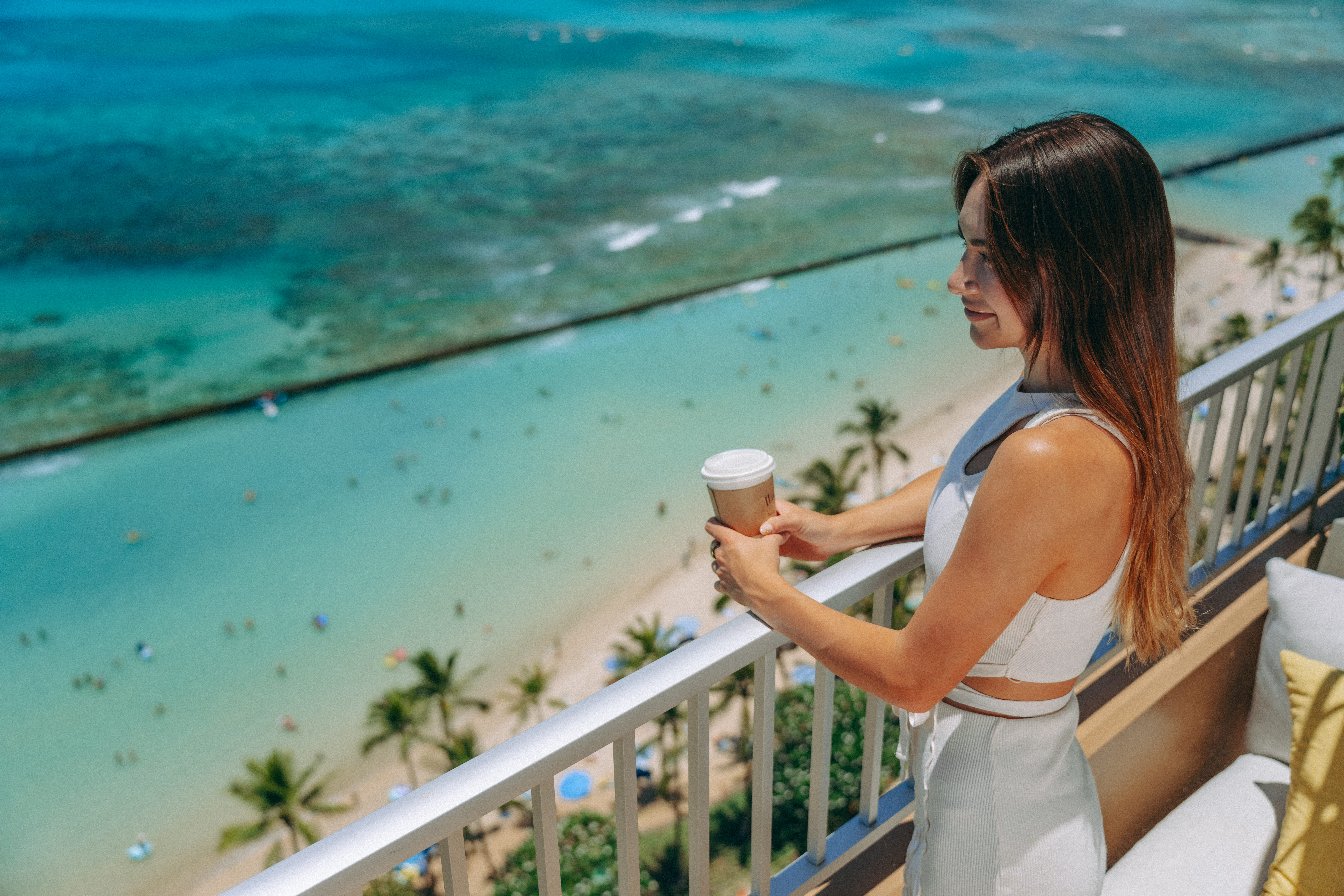 A woman stands on a balcony overlooking a beach and ocean.